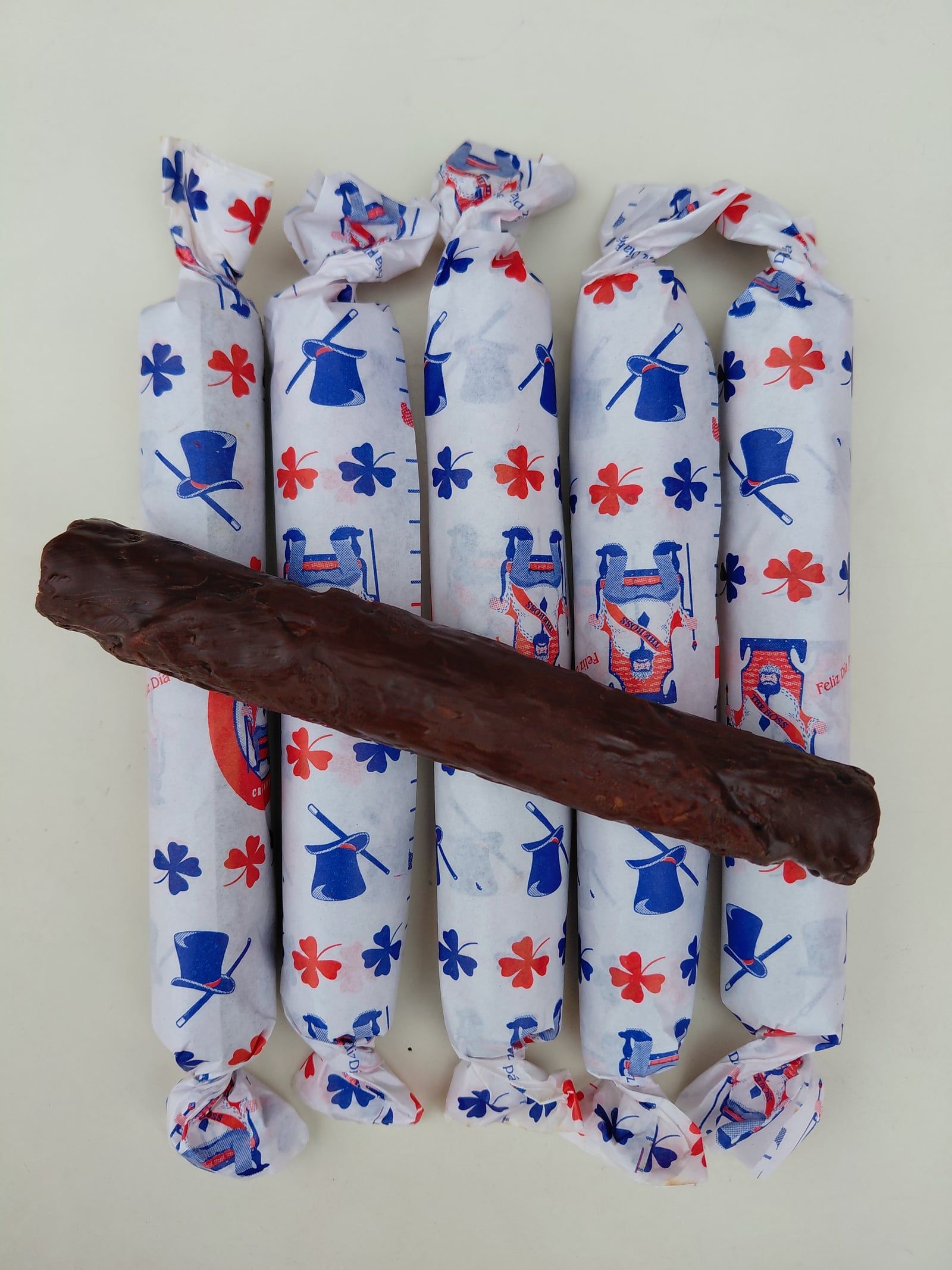Five habanitos in blue and red patterned wrappers with one unwrapped chocolate-coated habanito on top