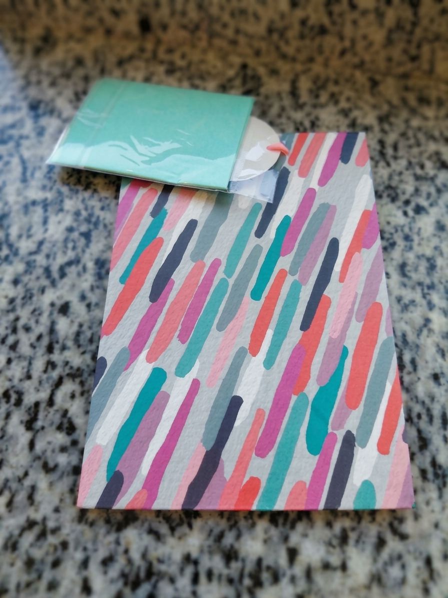 A gift bag with colorful brushstroke stripes, with mint tissue paper and a round gift tag peeking out