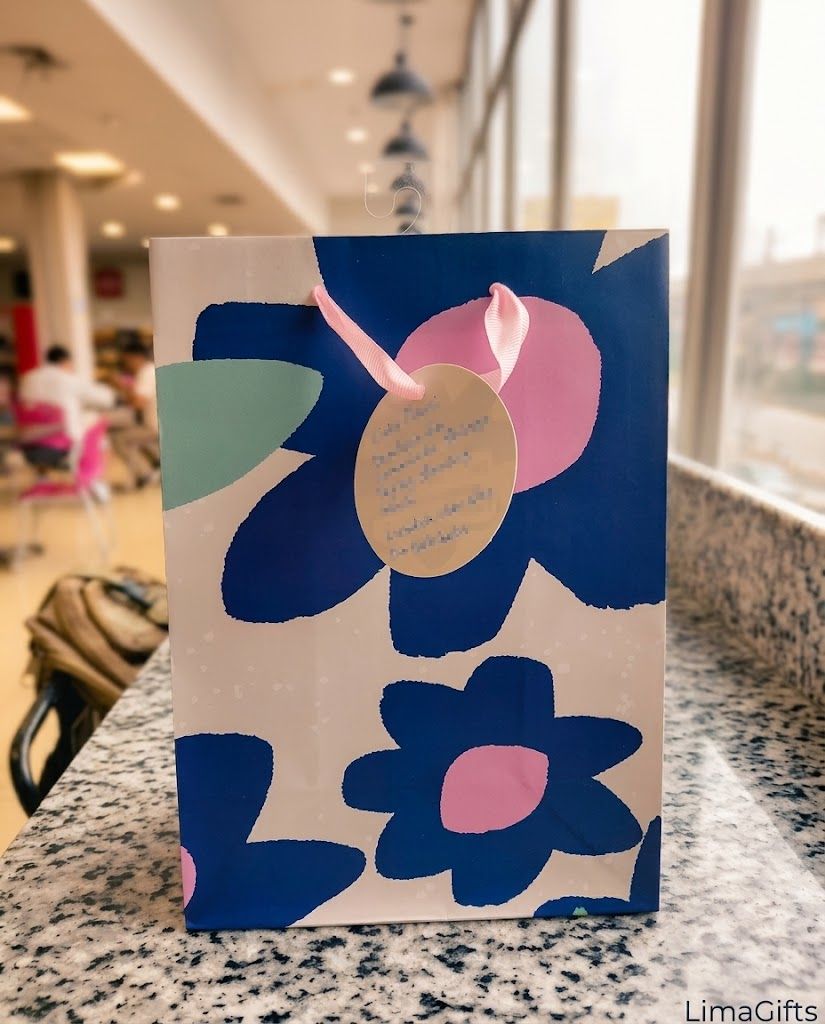 A gift bag with a blue and pink flower pattern, a pink ribbon and a handwritten card, delivered in Lima
