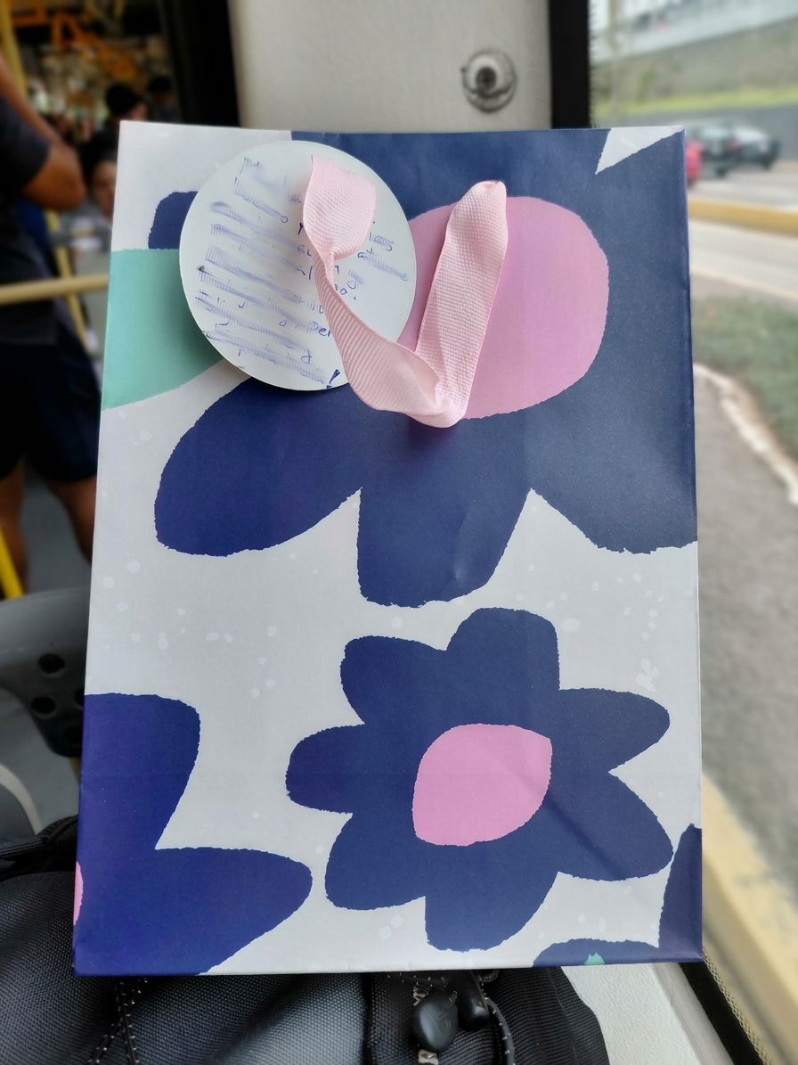 A navy gift bag with a pink and blue flower pattern, a pink ribbon and a handwritten card, delivered in Lima